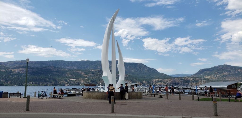 A waterfront plaza with a tall white abstract sculpture in the middle