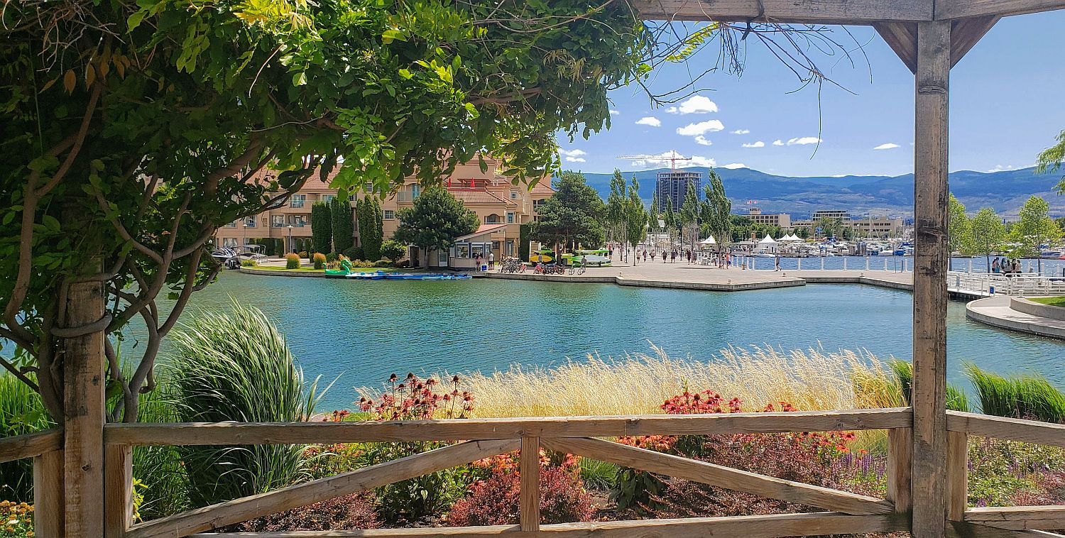 a planted arbour in the foreground looks over a lagoon and paved walkway in the background